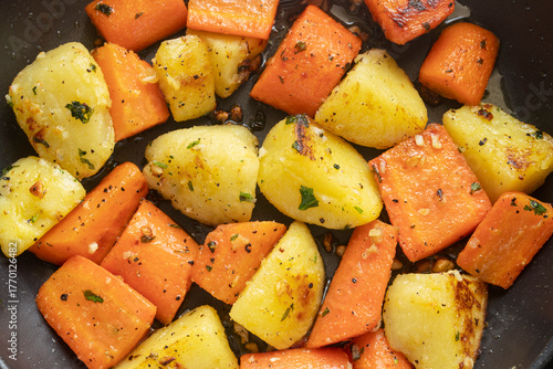 Pan-fried potatoes and carrots with garlic butter in hot pan.
