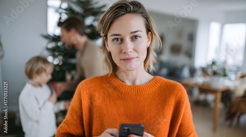 Woman holding smartphone with family decorating Christmas tree in cozy home