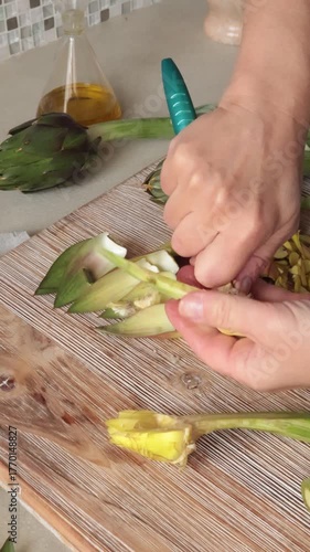 Anonymous person peels artichoke in kitchen at home. Healthy eating and traditional Italian dish. Fresh seasonal farm produce.