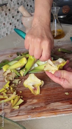 Anonymous person peels artichoke in kitchen at home. Healthy eating and traditional Italian dish. Fresh seasonal farm produce.