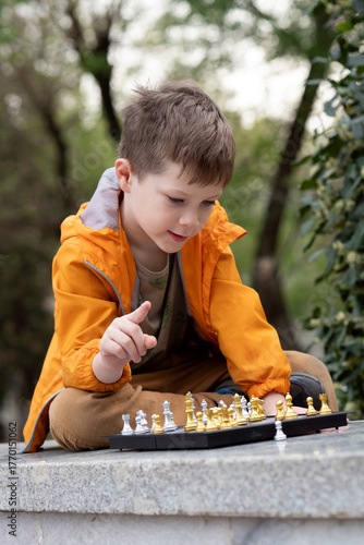 Boy playing chess outdoor. Learning strategic game. Education.