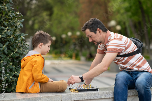 Boy with father playing chess outdoor. Learning strategic game. Education.