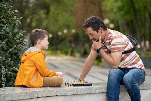 Boy with father playing chess outdoor.