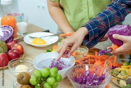 Hands of asian senior mother and adult daughter preparing healthy vegetable salad cutting cabbage carrots together in kitchen showing teamwork love freshness and family bonding lifestyle at home