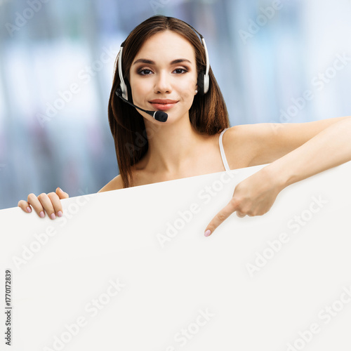 Call center. Customer support callcenter service phone operator, sale agent in microphone headset stand behind white signboard with free text space, against blurred office background. Ad concept image