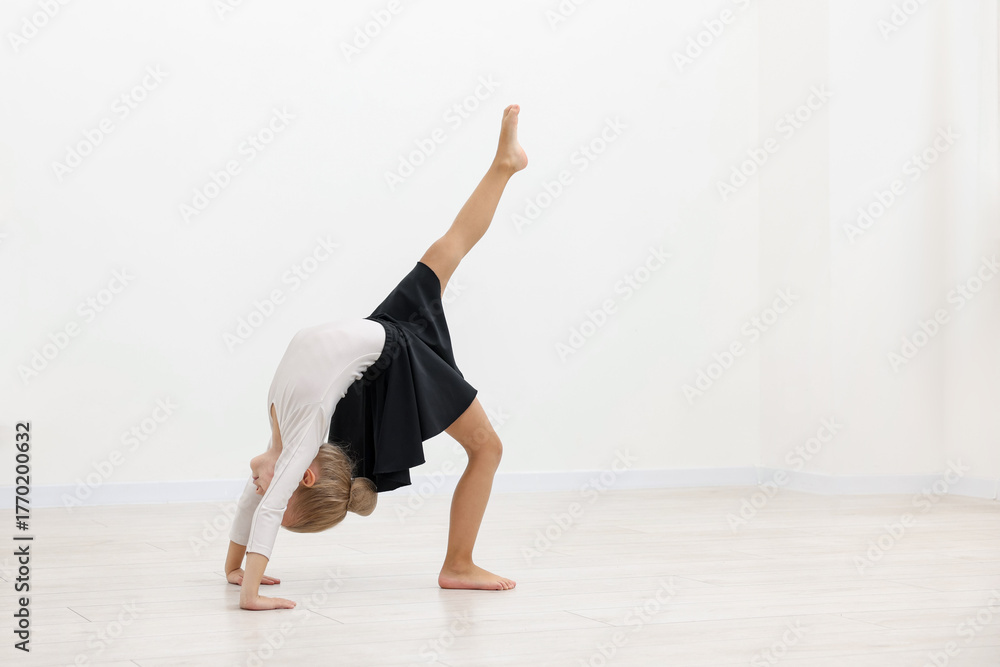 Naklejka premium Little girl doing gymnastic exercise on floor near white wall indoors. Space for text