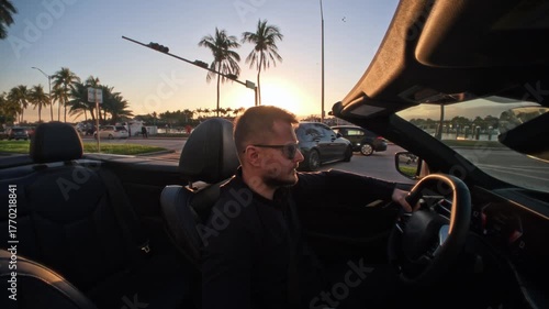 Relaxed tourist man wearing sunglasses driving a white convertible car through Miami at golden sunset. Sun flare creates cinematic atmosphere. Concept of travel, luxury lifestyle, freedom, and success