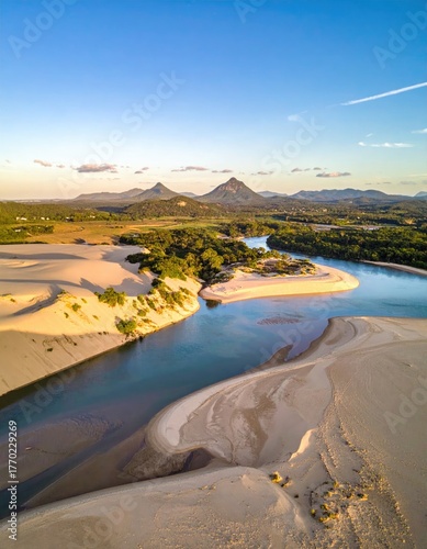 Aerial view of a river flowing through sand dunes, mountains in background