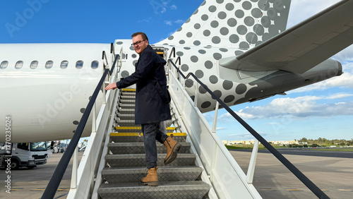 Ascending stairs to polka-dotted plane, Caucasian man in adventure boots, embodies Wanderlust Day spirit and global nomad vibe