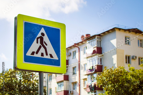 Road sign pedestrian crossing a background of city houses. Close-up, selective focus.