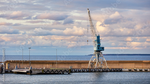 Industrial seaport landscape with a large cargo crane on a pier against a cloudy sky over the Baltic Sea. Calm water, concrete structures, maritime transport and harbor infrastructure.