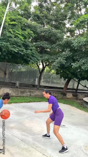 Two young women having fun while playing a one-on-one basketball game in a park
