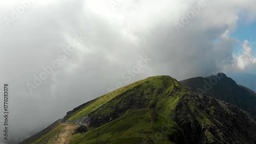 Magnificent mountain landscape, drone video. A big white fluffy cloud over the top of a mountain covered with lush green grass, a path in the mountains