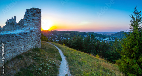 A beautiful panoramic view of Kremenets, Ukraine, at sunset, seen from the ruins of the medieval fortress on Bona Hill. A path leads along the old stone wall.