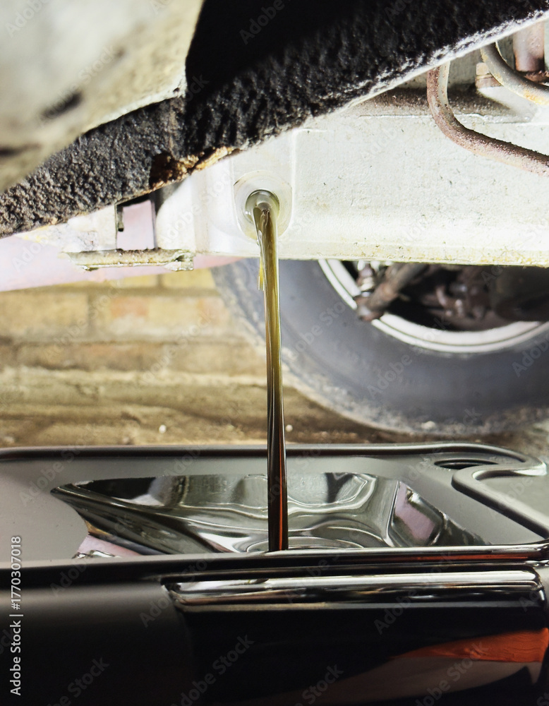 Φωτογραφία Closeup of old oil flowing from an engine sump into a pan container below, as part of an oil change service