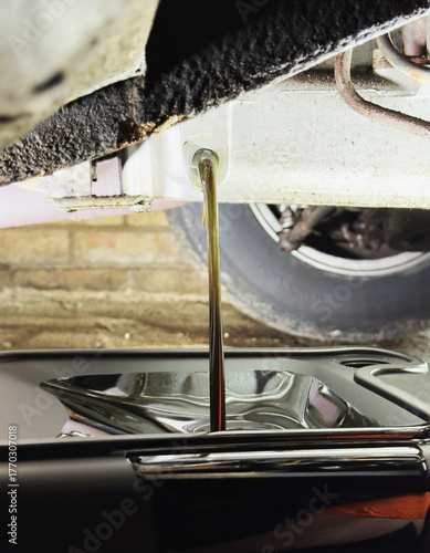 Closeup of old oil flowing from an engine sump into a pan container below, as part of an oil change service.