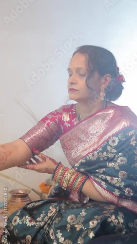 An Indian woman in a blue saree offering puja with a traditional thali during a festival