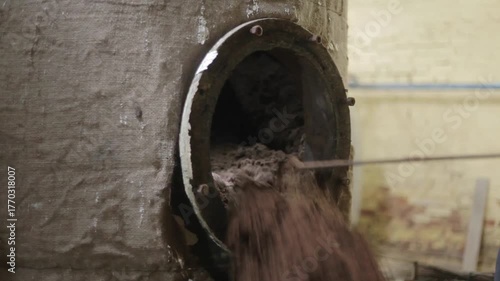 Worker cleaning biomass (plant residue) from industrial distillation chamber after essential oil extraction