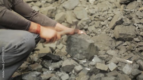 Worker crushing hard coal pieces with a hammer in an industrial environment