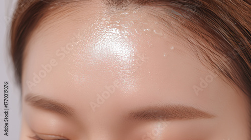 Close up of asian female forehead with dewy skin and visible cream application, highlighting smooth texture, healthy glow, and skincare routine in bright, clean setting