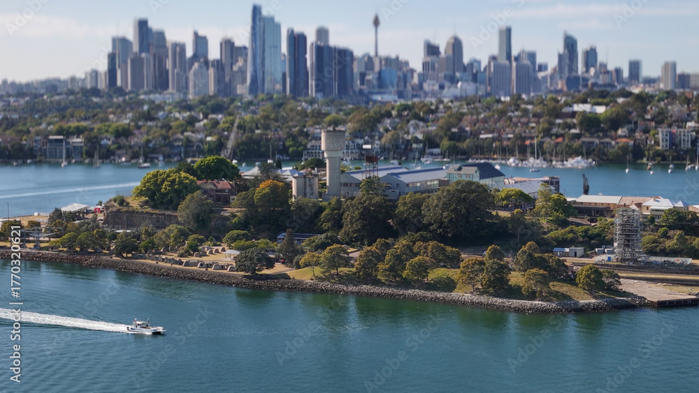 Naklejka premium Aerial drone view of Cockatoo Island on Parramatta River and Sydney Harbour, in Sydney, NSW Australia in October 2025 with Sydney City lens blur in the background