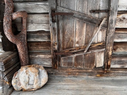 Background: door of a small, rustic wooden cabin with wood paneling, a wooden floor, a wooden sculpture, and a large stone in the corner to the left of the entrance.