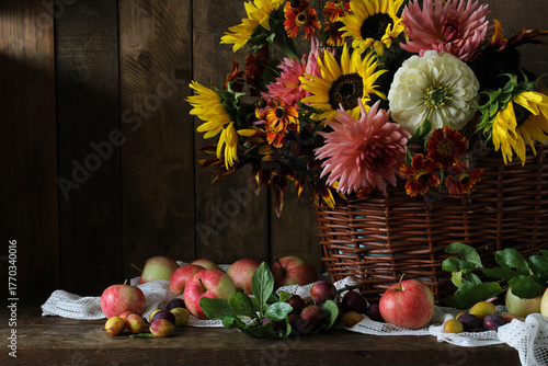 rural still life with a bouquet in a basket, garden apples and plums on a dark wooden background