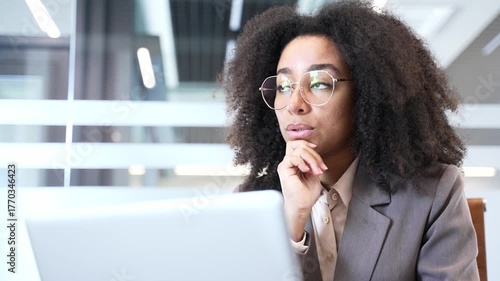 Thoughtful African American businesswoman thinking about problem solving while working on laptop at workplace in business office. Focused female manager deals with project, busy with tasks. Close up