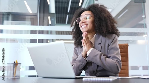 Happy excited african american businesswoman reading great news on laptop computer sitting at desk at workplace in business office. Joyful black woman celebrates success after receiving a good message
