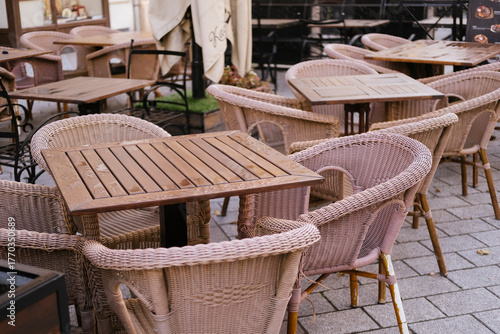 Cafe chairs and tables on outdoor wicker terrace patio, empty arrangement of wooden furniture at sidewalk bistro, cozy dining scene for morning relaxation and urban hospitality.