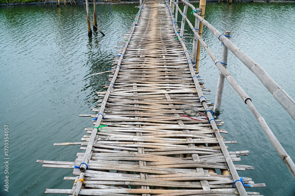 Fototapeta premium Rustic charm is captured in this old, weathered bamboo bridge stretching across tranquil waters. The detailed textures and simple construction evoke a sense of serenity and rural escape.