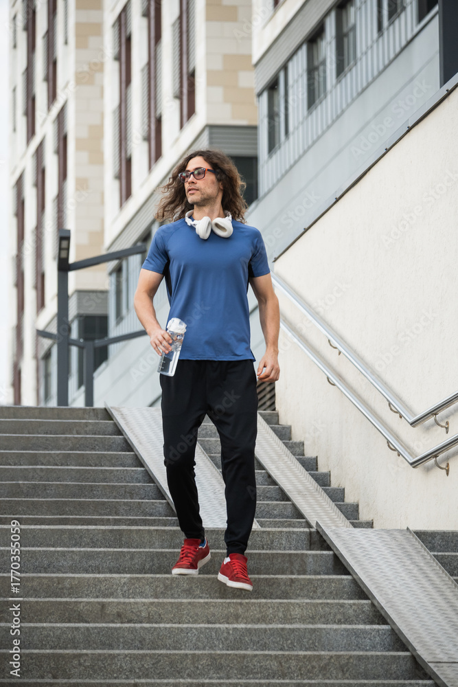 Naklejka premium Sporty man and athlete wearing blue t-shirt running at stair in modern city. Cardio workout training. Back view. Healthy lifestyle. Wellness