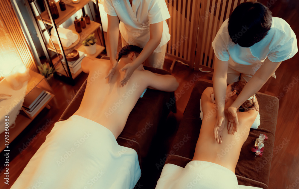 Obraz premium Caucasian couple customer enjoying relaxing anti-stress spa massage and pampering with beauty skin recreation leisure in warm candle lighting ambient salon spa at luxury resort or hotel. Quiescent