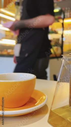 A yellow cup and teapot with tea are on the cafe table.A waiter walks past the table.Blurred background of the cafe interior.Vertical video. High quality 4k footage