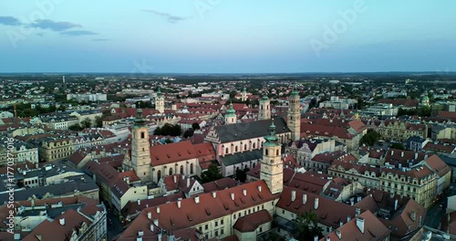 Aerial view of a European city with red-tiled roofs, churches, and buildings under a cloudy sky.