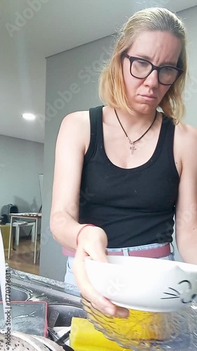 A young woman washes dishes in a modern kitchen, captured in time-lapse style. Concept of daily routine, home chores, cleaning, and domestic life