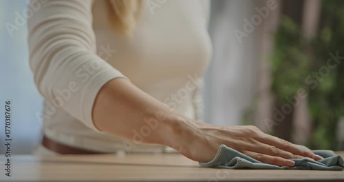 Close up of a woman hand wiping a wooden table with a light blue cloth while cleaning in a cozy home setting. Slow motion.