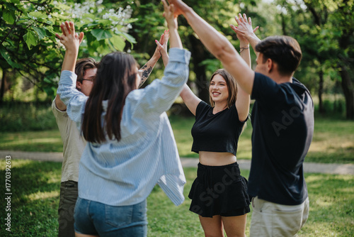 Carta da parati A cheerful group of four young adults laughing and playing together outdoors in a park, showcasing camaraderie and energy on a beautiful sunny day amidst lush greenery
