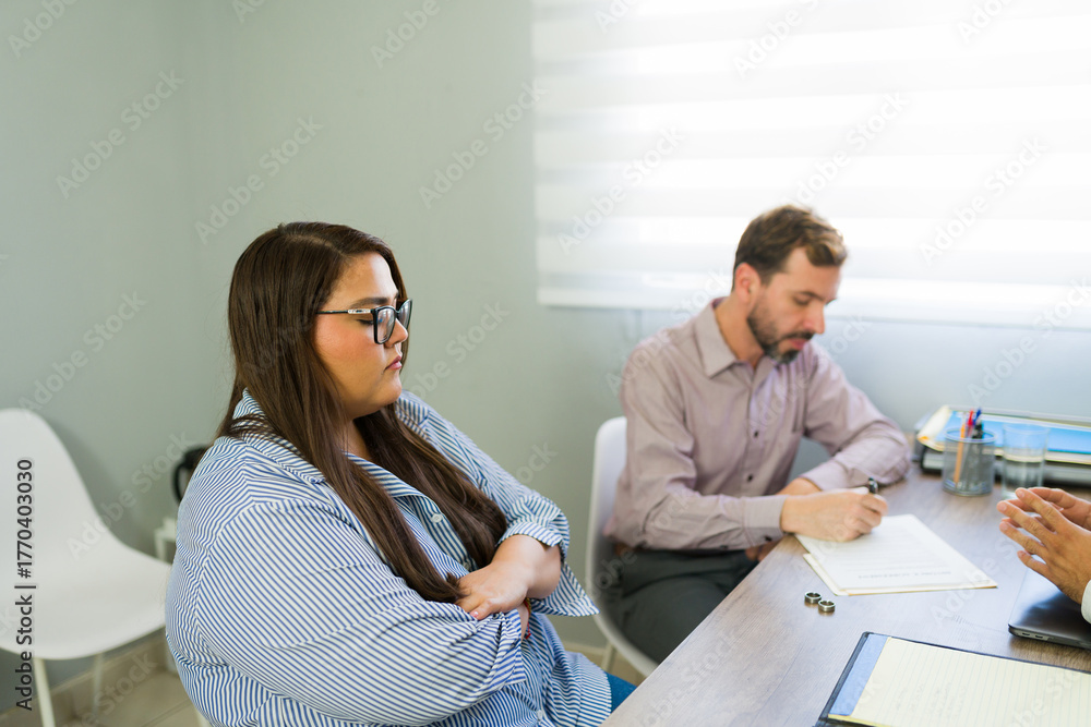 Fototapeta premium Sad couple signing divorce papers with lawyer in office