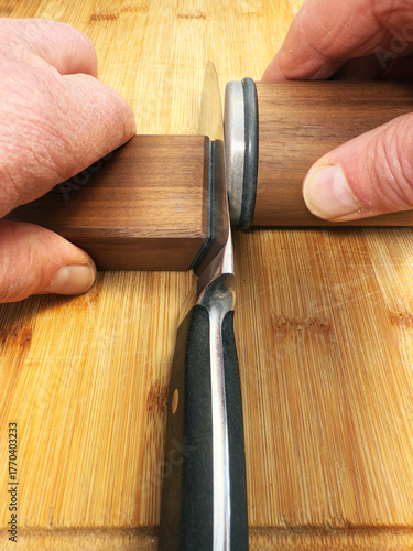 Принти на полотні Closeup of hands using a modern knife sharpener, consisting of a magnetic wooden block to hold the knife, while a disc is rolled along the blade length to sharpen it