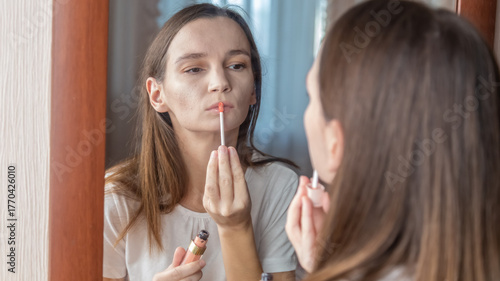 Young woman applying lipstick near mirror in bedroom