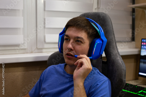 Gamer wearing gaming headphones engages in thoughtful conversation with teammates while discussing game strategy. Authentic moment in real gaming environment, showcasing focused emotions of gameplay