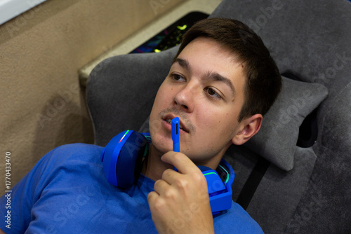 Young gamer has removed his blue gaming headphones but is using microphone to communicate with other players, reflecting moment of interaction during intense gaming session