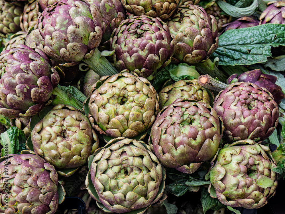 Obraz premium Fresh Purple And Green Artichokes Piled In A Market Display For Cooking And Healthy Meals