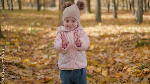 A child's outdoor portrait in red and yellow leaves in an autumn park. Autumn and mood. A beautiful portrait of a sweet girl on a beautiful autumn day.Little girl clapping her hands, smiling.