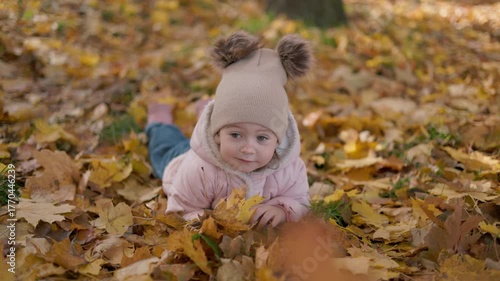 Beautiful girl with an autumn leaf in her hands. Adorable child playing in leaves on an autumn day.