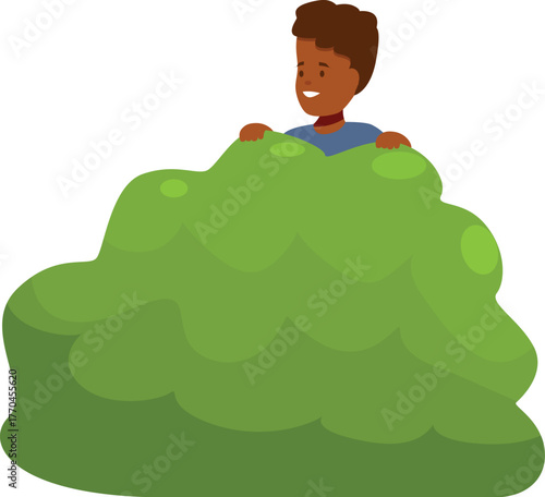 Smiling boy hiding in green bush, playing hide and seek in the park