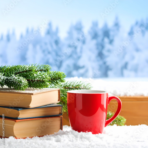 Stack of books and red cup in front of a snowy winter landscape