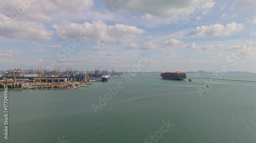 Wide aerial view showing a large cargo container ship entering Laem Chabang Port in Chonburi, Thailand, with cranes and docked vessels.