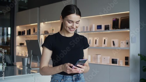 Young beautiful woman smiling while using her smartphone in a tech handheld device gadget store location background